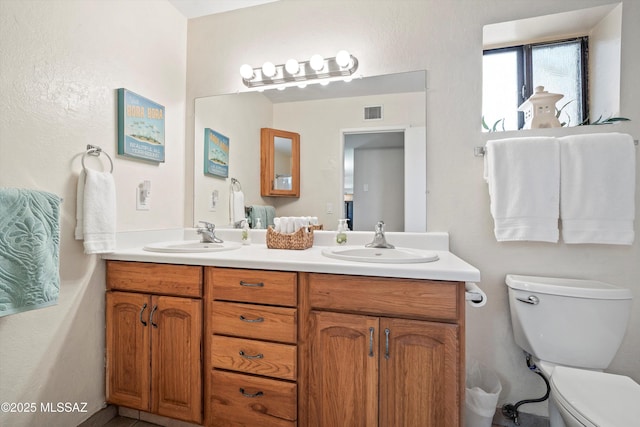 full bathroom featuring visible vents, double vanity, a sink, and toilet