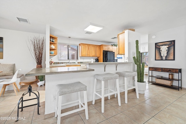 kitchen with a peninsula, a breakfast bar, a sink, visible vents, and freestanding refrigerator