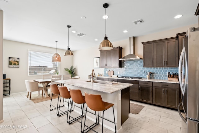 kitchen with visible vents, wall chimney exhaust hood, stainless steel appliances, dark brown cabinets, and backsplash