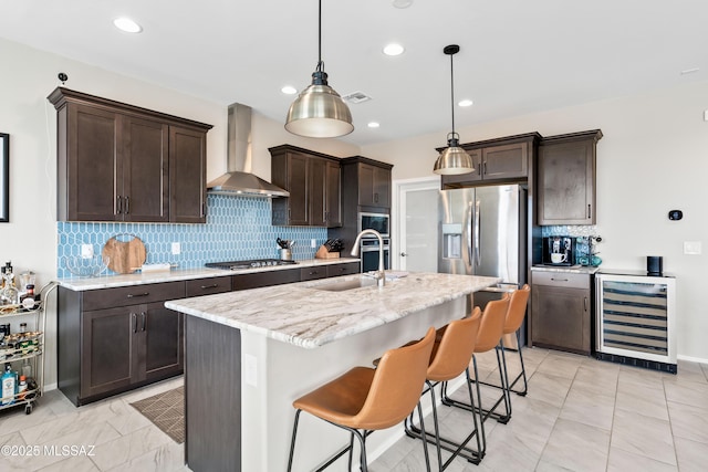 kitchen with dark brown cabinetry, wine cooler, appliances with stainless steel finishes, wall chimney range hood, and a sink