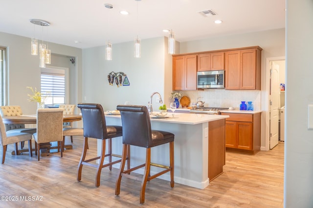 kitchen featuring a breakfast bar area, visible vents, light countertops, decorative backsplash, and stainless steel microwave