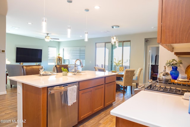 kitchen featuring light wood-style flooring, a sink, stainless steel dishwasher, brown cabinets, and a center island with sink