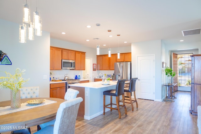 kitchen featuring a breakfast bar, light countertops, light wood-style flooring, appliances with stainless steel finishes, and a kitchen island with sink