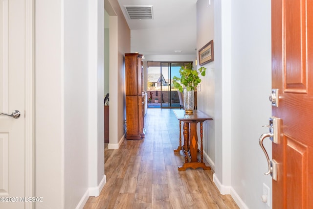 hall featuring baseboards, visible vents, and light wood-style floors