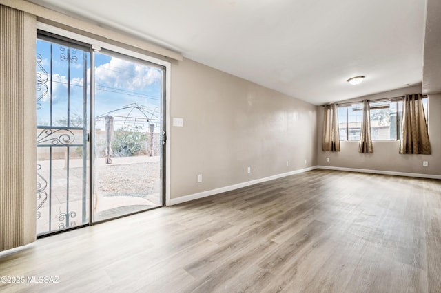 empty room featuring lofted ceiling, baseboards, and wood finished floors