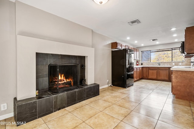 kitchen with visible vents, brown cabinetry, a tile fireplace, light countertops, and black appliances