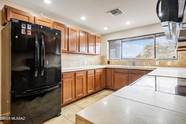 kitchen featuring tasteful backsplash, visible vents, brown cabinets, freestanding refrigerator, and a sink