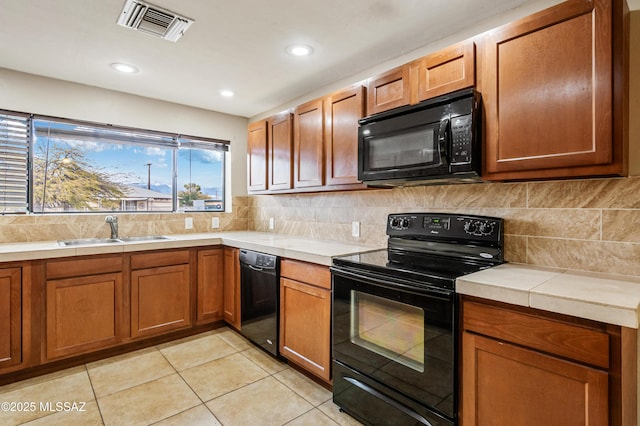 kitchen featuring visible vents, decorative backsplash, light countertops, black appliances, and a sink