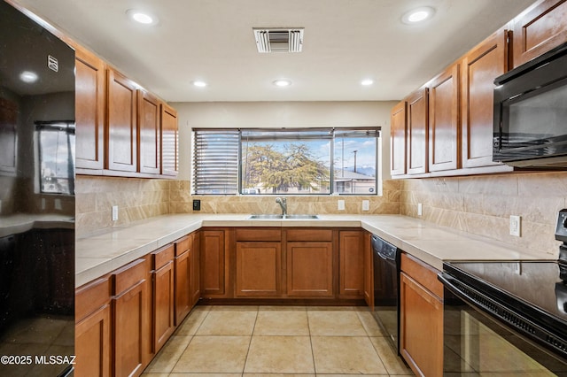 kitchen featuring a sink, visible vents, decorative backsplash, black appliances, and brown cabinetry