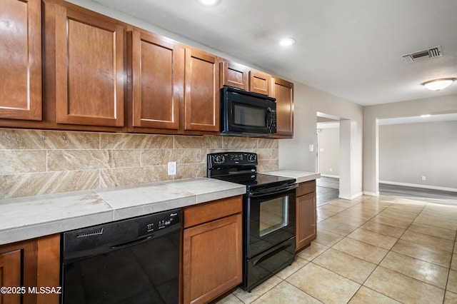 kitchen with tasteful backsplash, visible vents, brown cabinets, black appliances, and light tile patterned flooring