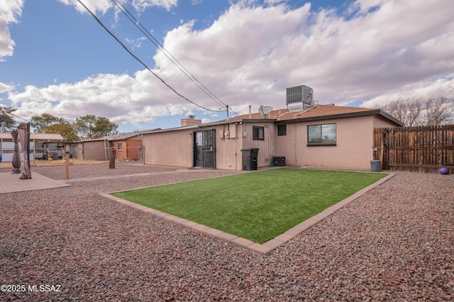 rear view of house featuring a lawn, fence, central AC, and brick siding