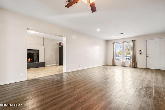 unfurnished living room featuring visible vents, a ceiling fan, wood finished floors, a tile fireplace, and baseboards