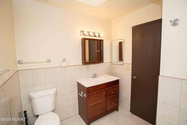 bathroom featuring tile patterned flooring, toilet, a wainscoted wall, vanity, and tile walls