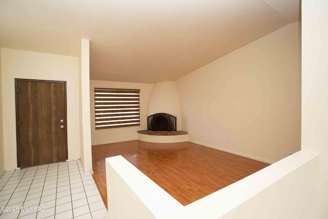 interior space featuring vaulted ceiling, a large fireplace, light wood-type flooring, and baseboards