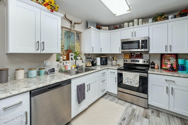 kitchen with light wood finished floors, white cabinetry, appliances with stainless steel finishes, and a sink