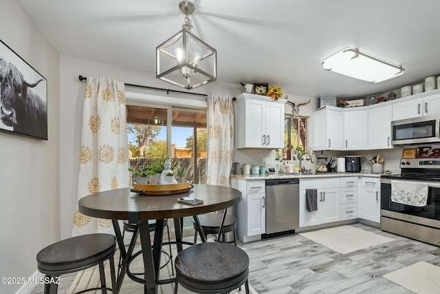 kitchen featuring a notable chandelier, a sink, white cabinetry, light countertops, and appliances with stainless steel finishes