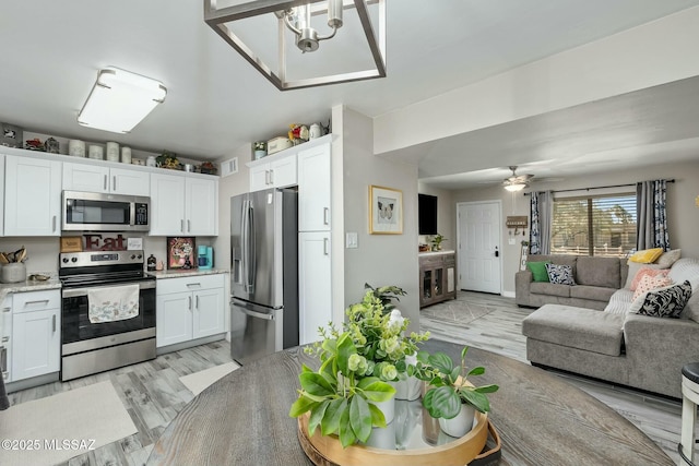 kitchen with appliances with stainless steel finishes, open floor plan, white cabinetry, and light wood finished floors