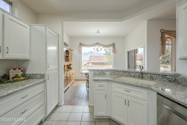 kitchen with light tile patterned floors, white cabinets, a sink, light stone countertops, and stainless steel dishwasher