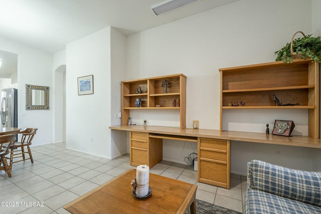 home office with light tile patterned floors, baseboards, arched walkways, and built in study area