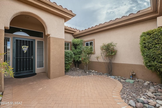 doorway to property featuring a tile roof, a patio area, and stucco siding