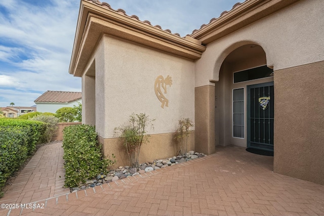 property entrance with a patio area, a tile roof, and stucco siding