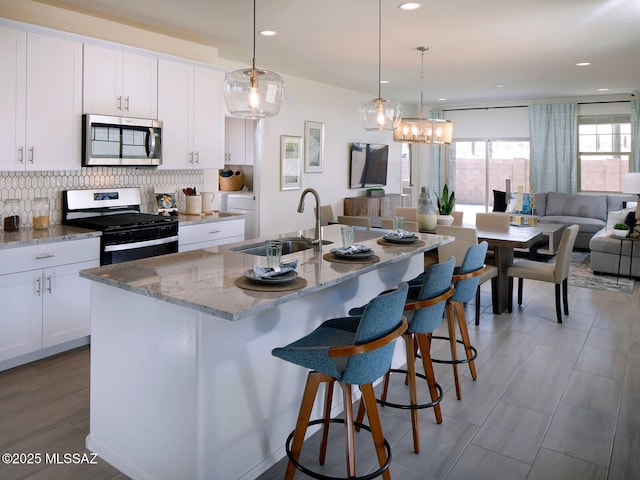 kitchen featuring a sink, white cabinetry, open floor plan, appliances with stainless steel finishes, and decorative backsplash