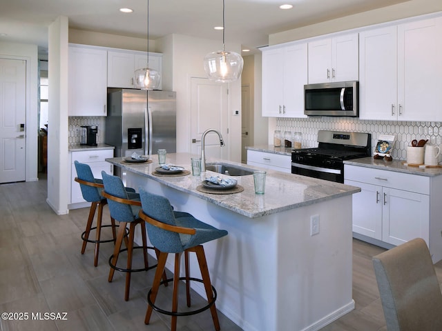 kitchen featuring a kitchen island with sink, stainless steel appliances, a sink, white cabinetry, and backsplash