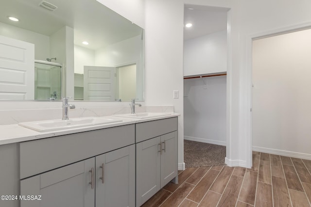 full bathroom featuring visible vents, a spacious closet, wood finish floors, a shower stall, and a sink