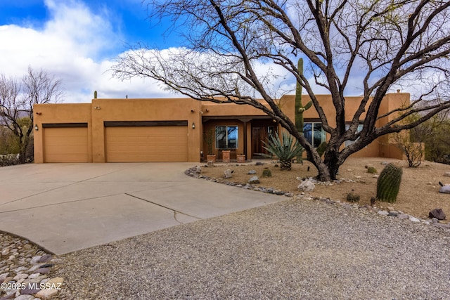 adobe home featuring an attached garage, driveway, and stucco siding