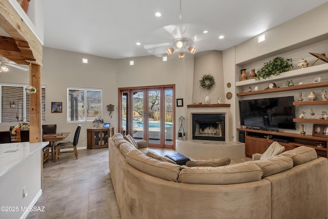 living room featuring a fireplace with raised hearth, built in shelves, ceiling fan, recessed lighting, and french doors