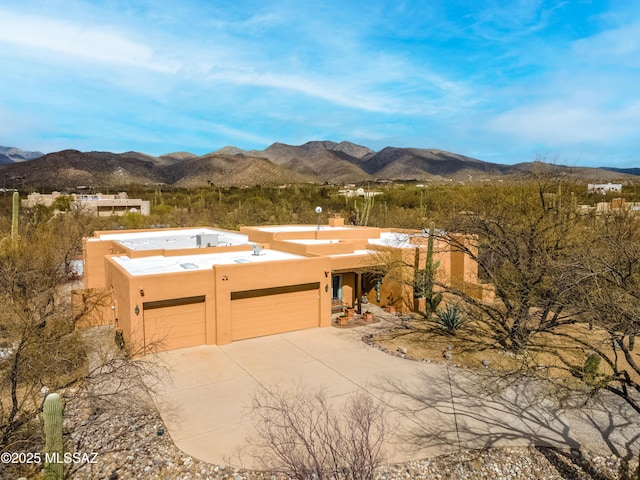 adobe home featuring a garage, a mountain view, driveway, and stucco siding