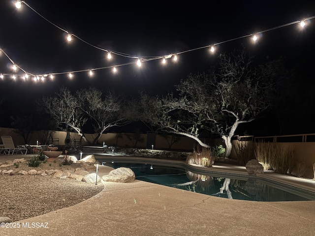 pool at night with a fenced in pool, a fenced backyard, and a patio area