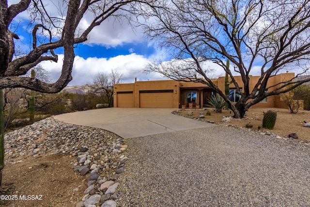 pueblo-style house featuring a garage, driveway, and stucco siding