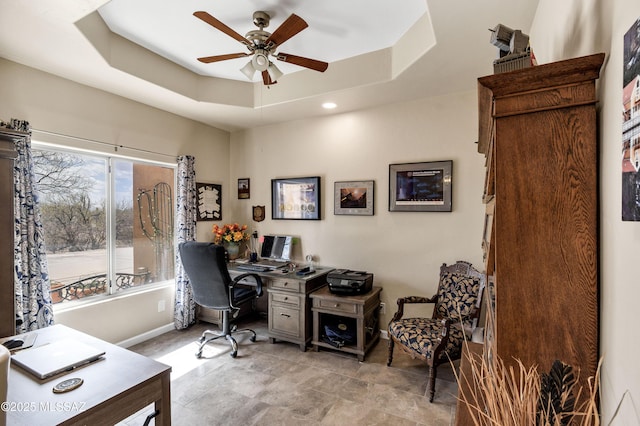 home office featuring a raised ceiling, a ceiling fan, and baseboards