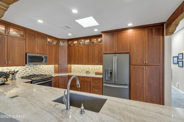 kitchen with visible vents, a sink, appliances with stainless steel finishes, brown cabinetry, and light stone countertops