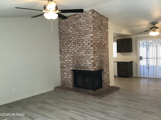 unfurnished living room with lofted ceiling, ceiling fan, light wood-style flooring, baseboards, and a brick fireplace