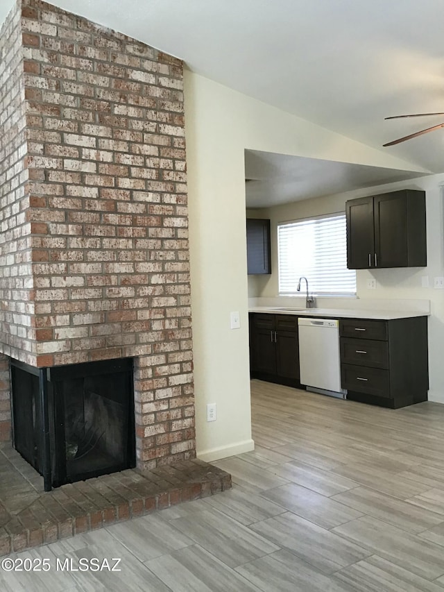 kitchen with baseboards, a fireplace, white dishwasher, a ceiling fan, and a sink