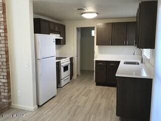 kitchen with a sink, white appliances, light wood-style floors, dark brown cabinetry, and light countertops