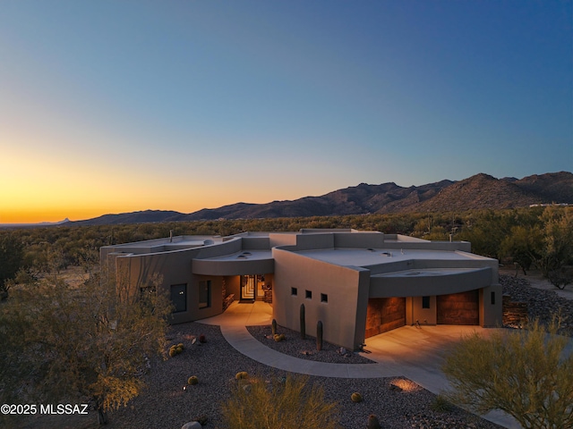 back of house at dusk with stucco siding, a mountain view, and a garage