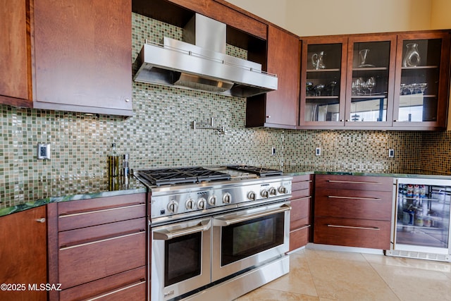 kitchen featuring backsplash, glass insert cabinets, wall chimney range hood, wine cooler, and range with two ovens