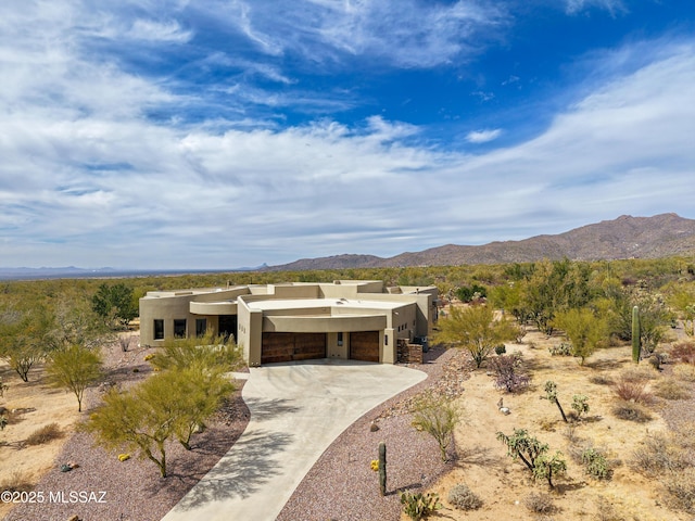 pueblo-style home with a garage, concrete driveway, a mountain view, and stucco siding