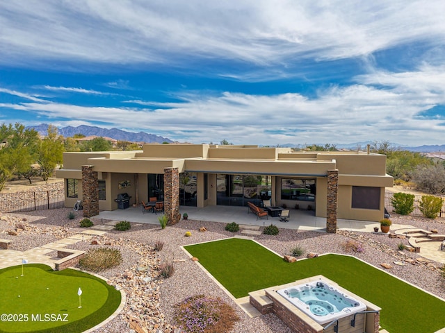 rear view of house with fence, stucco siding, an outdoor hot tub, a patio area, and a mountain view