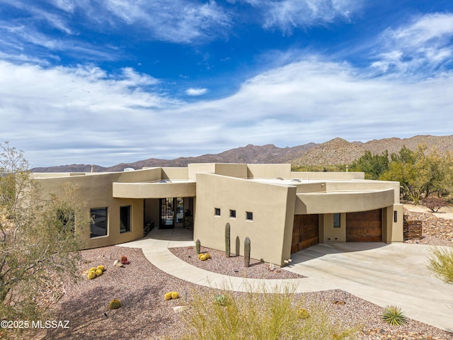 pueblo-style home with a mountain view, stucco siding, an attached garage, and driveway