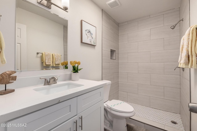 bathroom featuring toilet, visible vents, tiled shower, and vanity