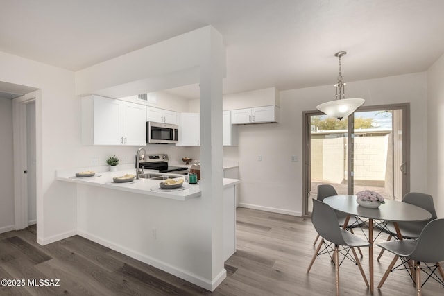 kitchen with appliances with stainless steel finishes, white cabinetry, a sink, wood finished floors, and a peninsula