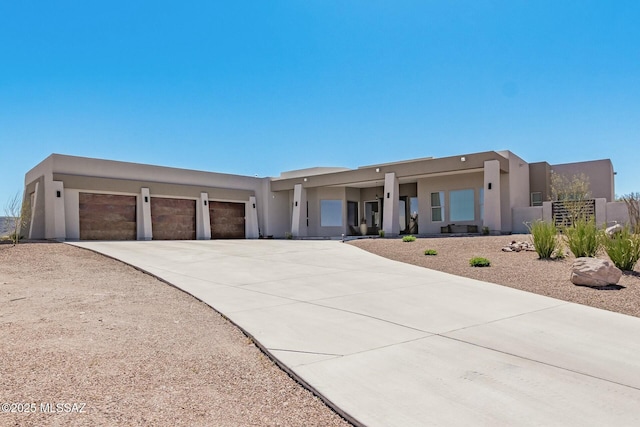 pueblo revival-style home featuring concrete driveway, an attached garage, and stucco siding