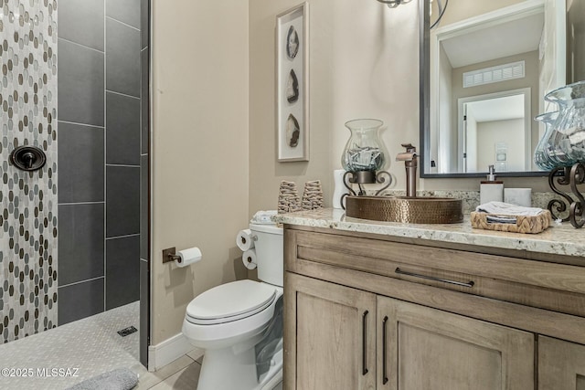 bathroom featuring tile patterned flooring, a tile shower, vanity, and toilet