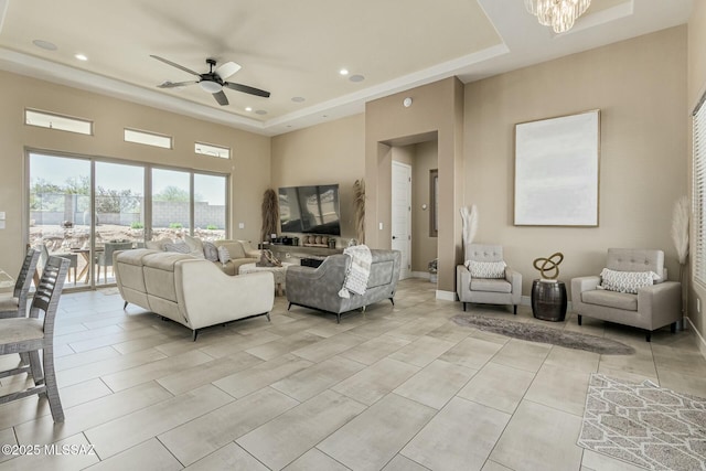 living room with baseboards, a towering ceiling, a tray ceiling, ceiling fan with notable chandelier, and recessed lighting