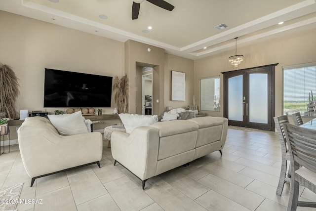 living room featuring a tray ceiling, light tile patterned floors, recessed lighting, visible vents, and ceiling fan with notable chandelier