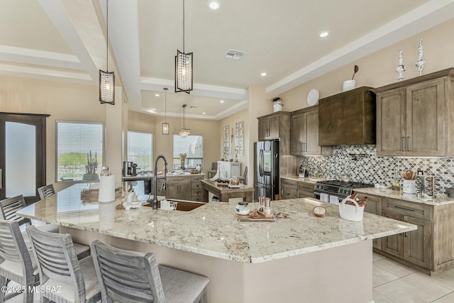 kitchen featuring visible vents, appliances with stainless steel finishes, a sink, a tray ceiling, and backsplash